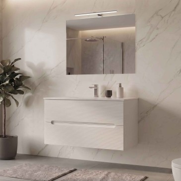 Meuble de salle de bain suspendu blanc laiteux avec finition côtelée, miroir et éclairage assortis.